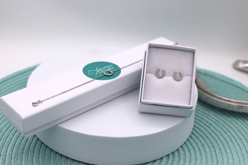 A sterling silver horseshoe bracelet and earring set, with the bracelet displayed on the bracelet's jewellery box and the earrings in a white jewellery box, all presented on a turquoise patterned surface.