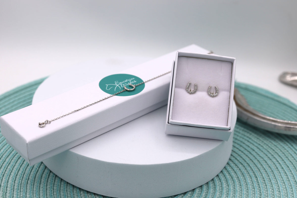 A sterling silver horseshoe bracelet and earring set, with the bracelet displayed on the bracelet's jewellery box and the earrings in a white jewellery box, all presented on a turquoise patterned surface.