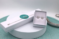 A sterling silver horseshoe bracelet and earring set, with the bracelet displayed on the bracelet's jewellery box and the earrings in a white jewellery box, all presented on a turquoise patterned surface.