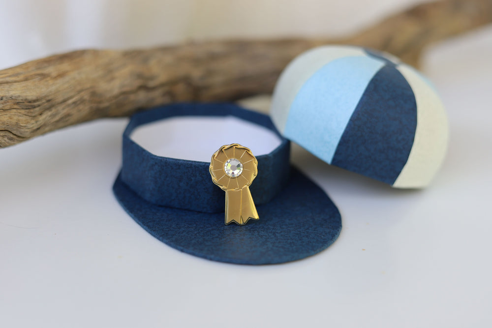 A gold-colored equestrian rosette pin next to it's display hat box