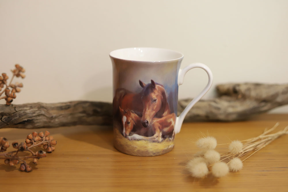 A coffee mug displaying a mare and her foal lying in a stable, 