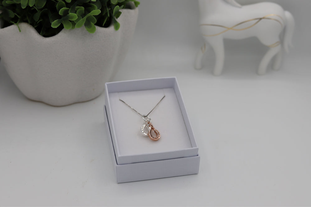 A sterling silver horseshoe pendant in a white gift box, with a Sterling silver rhodium plated chain. The pendant has one rose gold coloured horseshoe with one micron layer of pink gold.