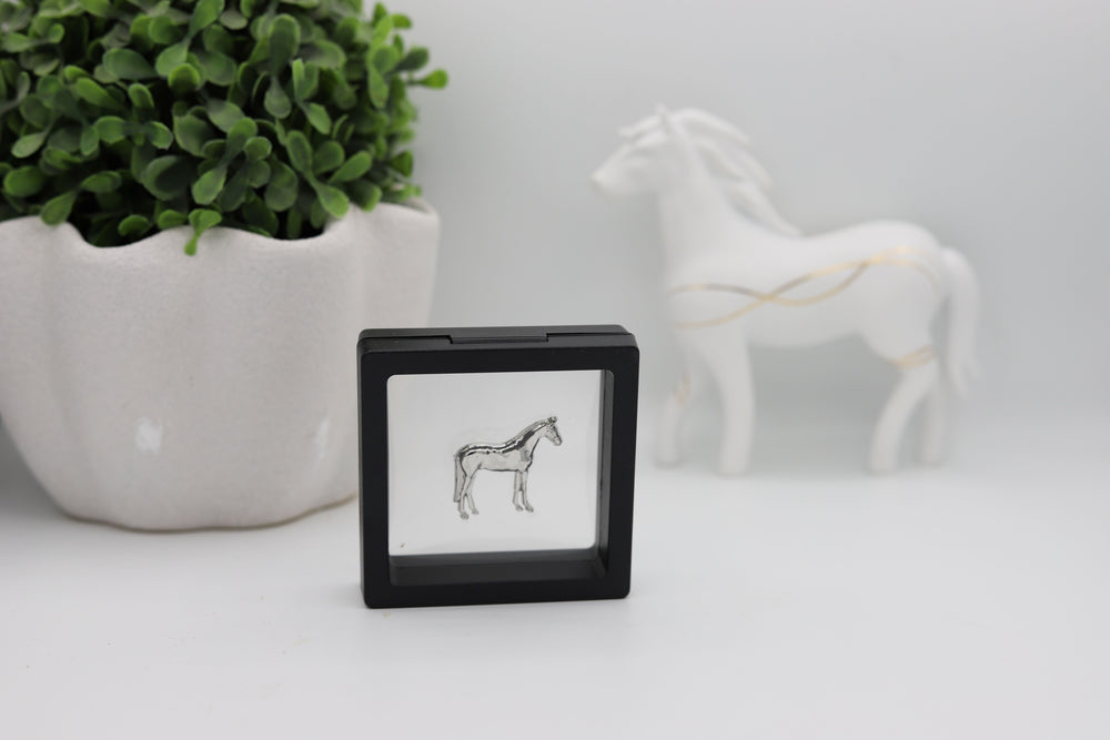 A silver-colored brooch pin shaped like a horse, displayed in a floating case