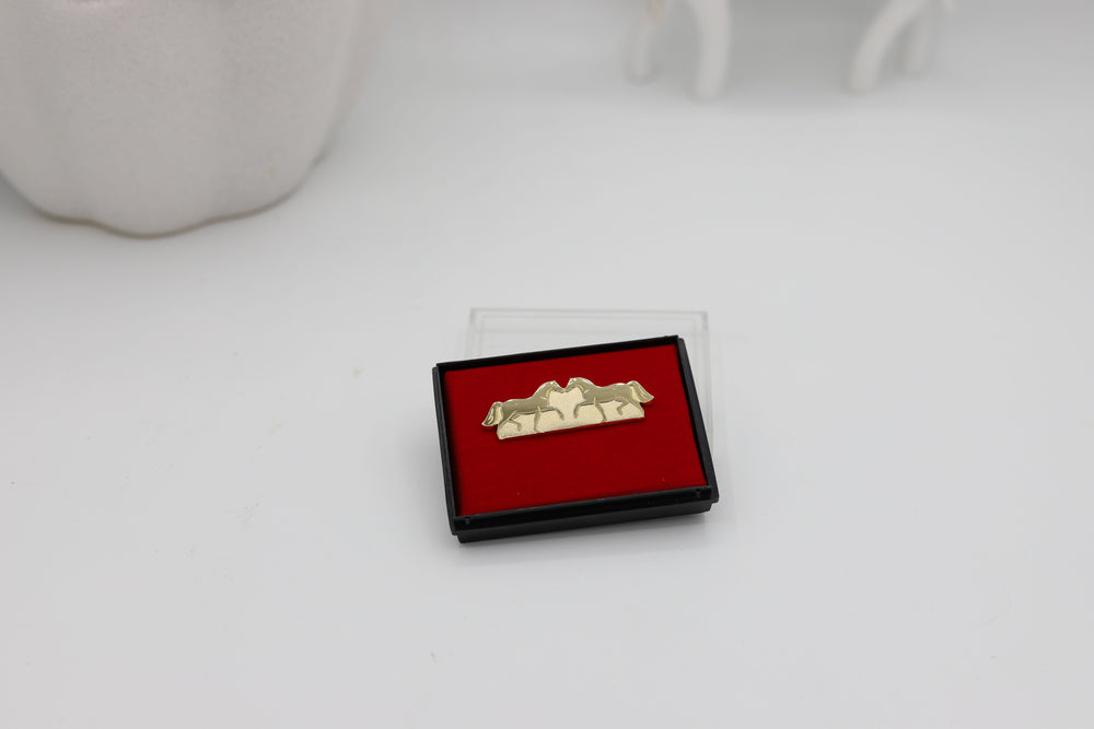 A gold-colored pin in the shape of two horses displayed on a red velvet surface