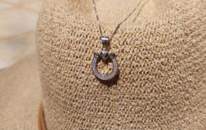 Sterling Silver Horseshoe and heart pendant on a sterling silver chain leaning on a woven beige hat as background 