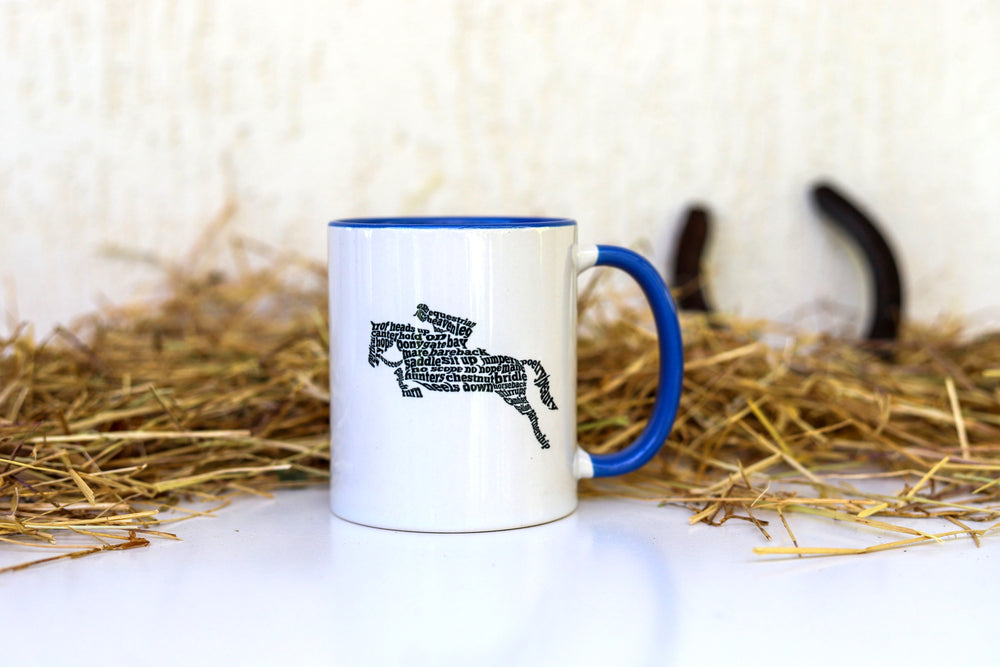 A white ceramic mug with blue trim, featuring an illustration of a horse and rider jumping made up of equestrian words - Equestrian gifts Australia